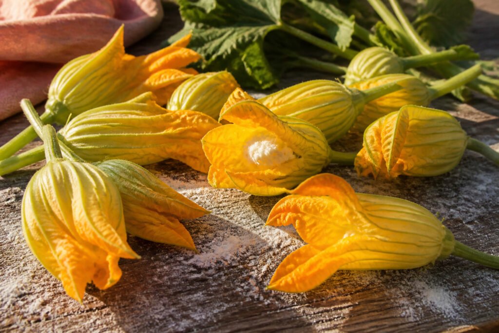 A wooden cutting board with freshly harvested zucchini flowers and a bowl of water.